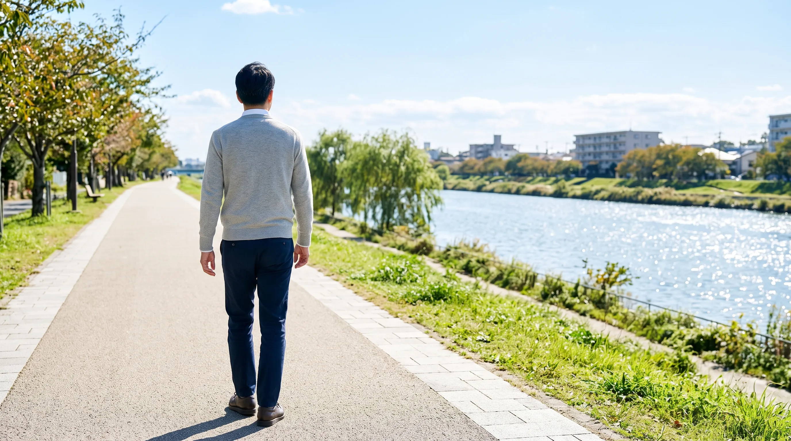 晴れた日、川沿いの明るい遊歩道を歩く男性の後ろ姿