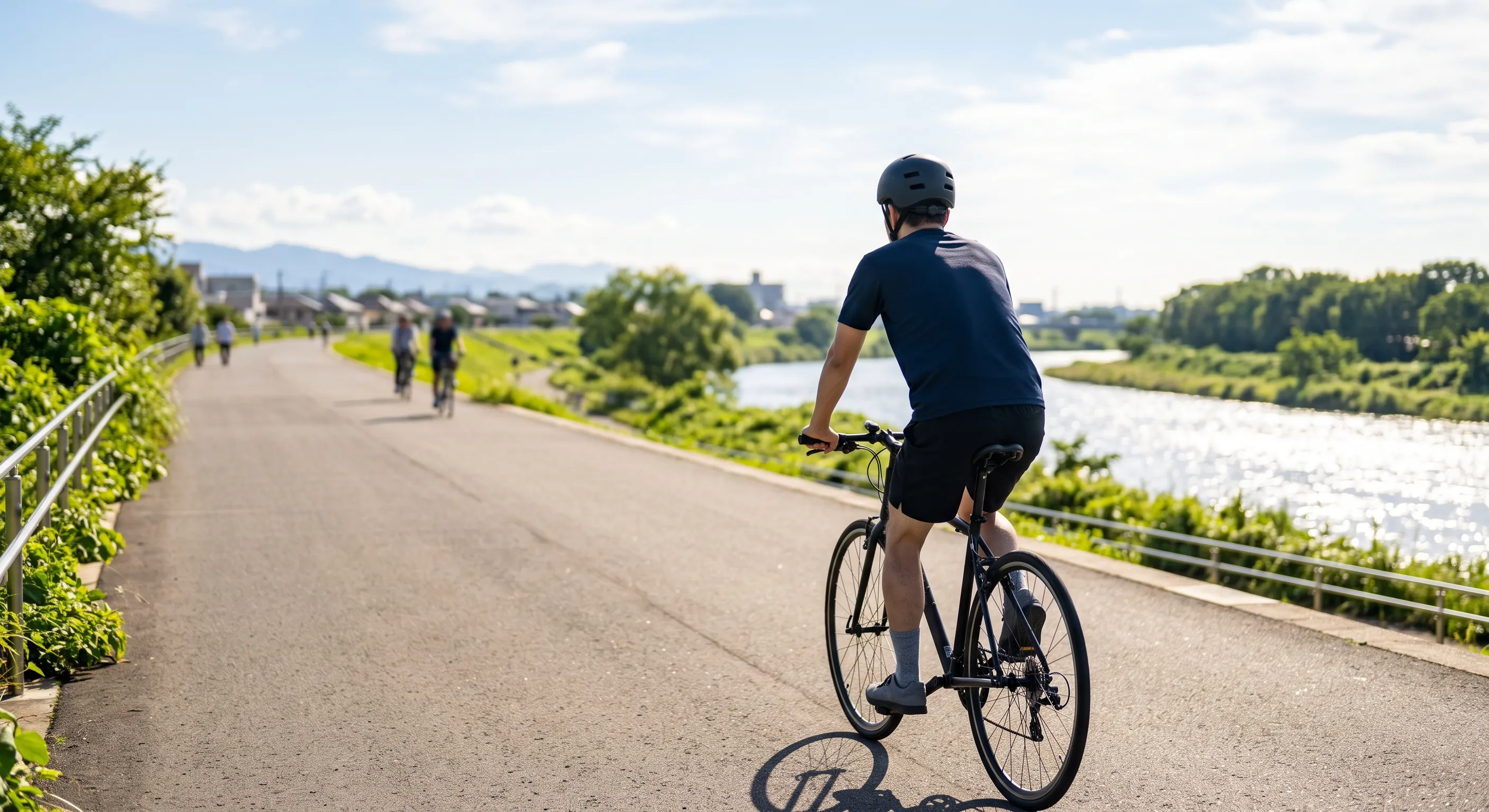 晴れた朝、川沿いの道を自転車で走る男性の後ろ姿